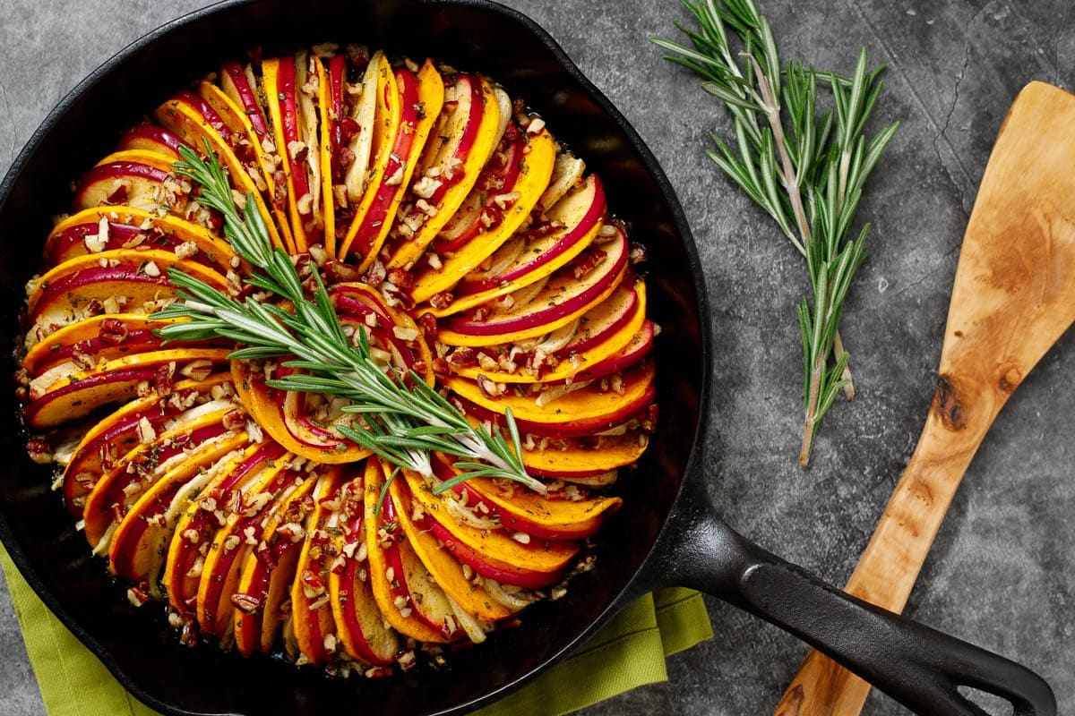 Butternut squash and apple tian with fennel and orange, served in a cast iron skillet. Extra rosemary and a wood serving spatula sit to the side.