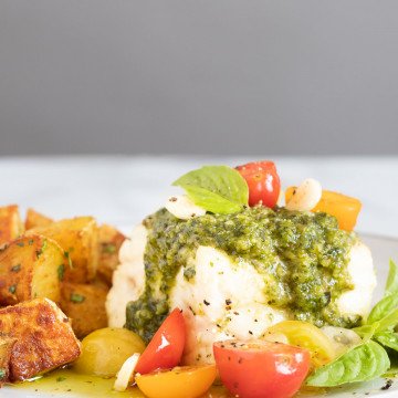 White fish with green pesto and red and yellow tomatoes on a plate with roasted potatoes