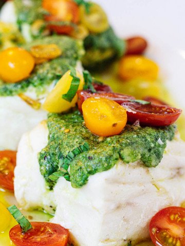 Pieces of sear-roasted halibut topped with macadamia nut pesto and tomatoes on a white plate