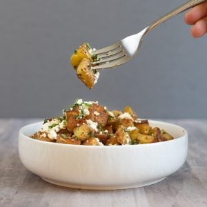 a bowl of crispy browned potatoes topped with white cheese and parsely