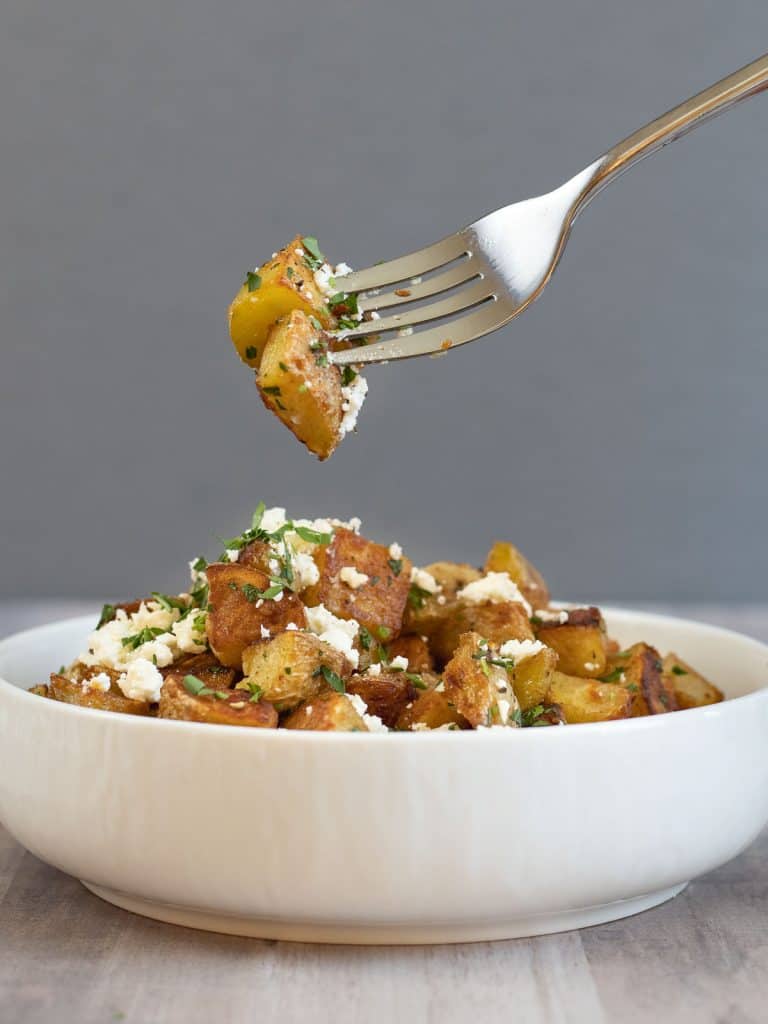 a bowl of crispy browned potatoes topped with white cheese and parsely