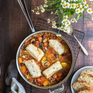 fish on a bed of cooked tomato sauce with olives and basil