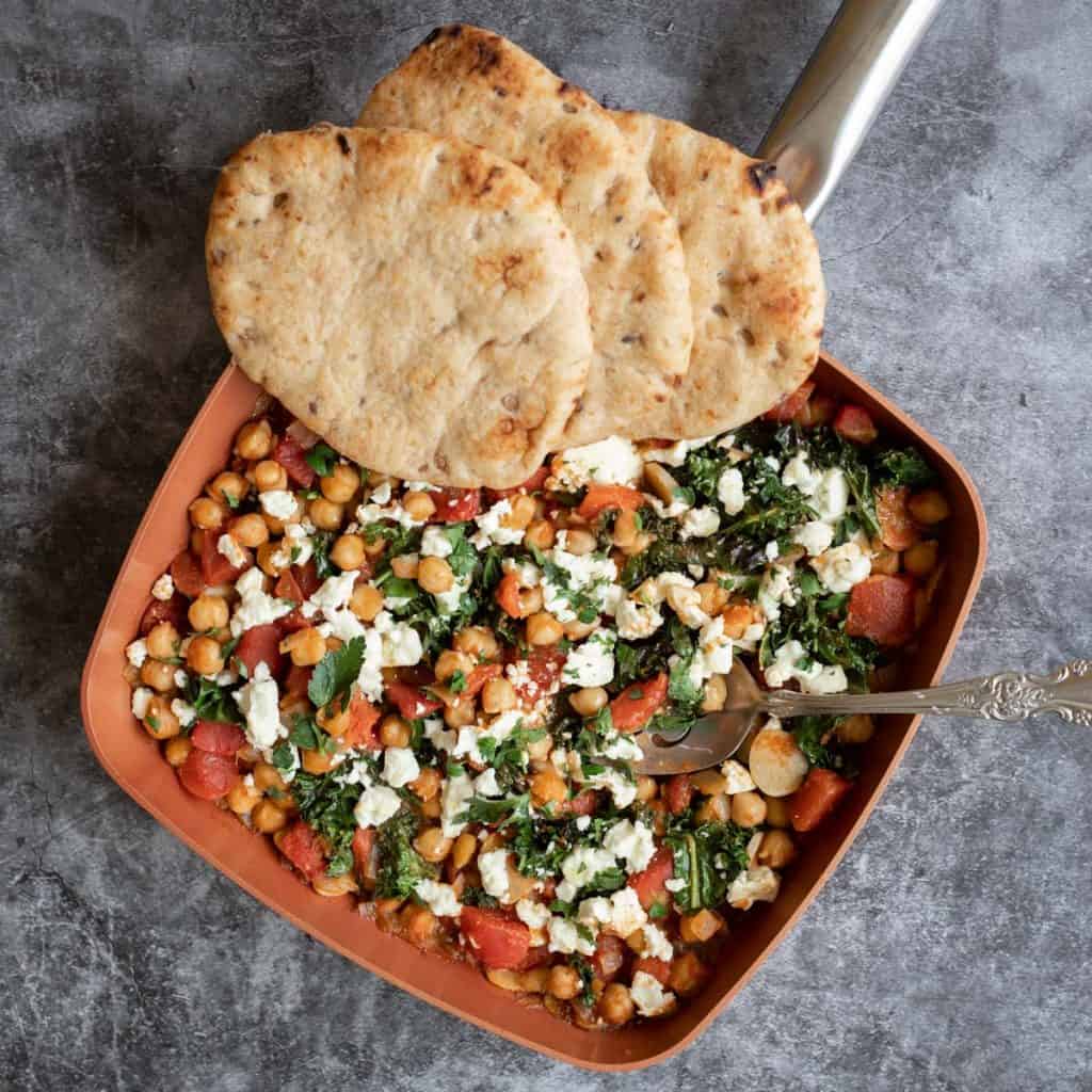 Mediterranean chickpea skillet with tomatoes, kale, and feta cheese and accompanied with whole grain pita bread.