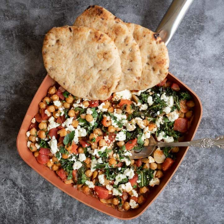 Mediterranean chickpea skillet with tomatoes, kale, and feta cheese and accompanied with whole grain pita bread.