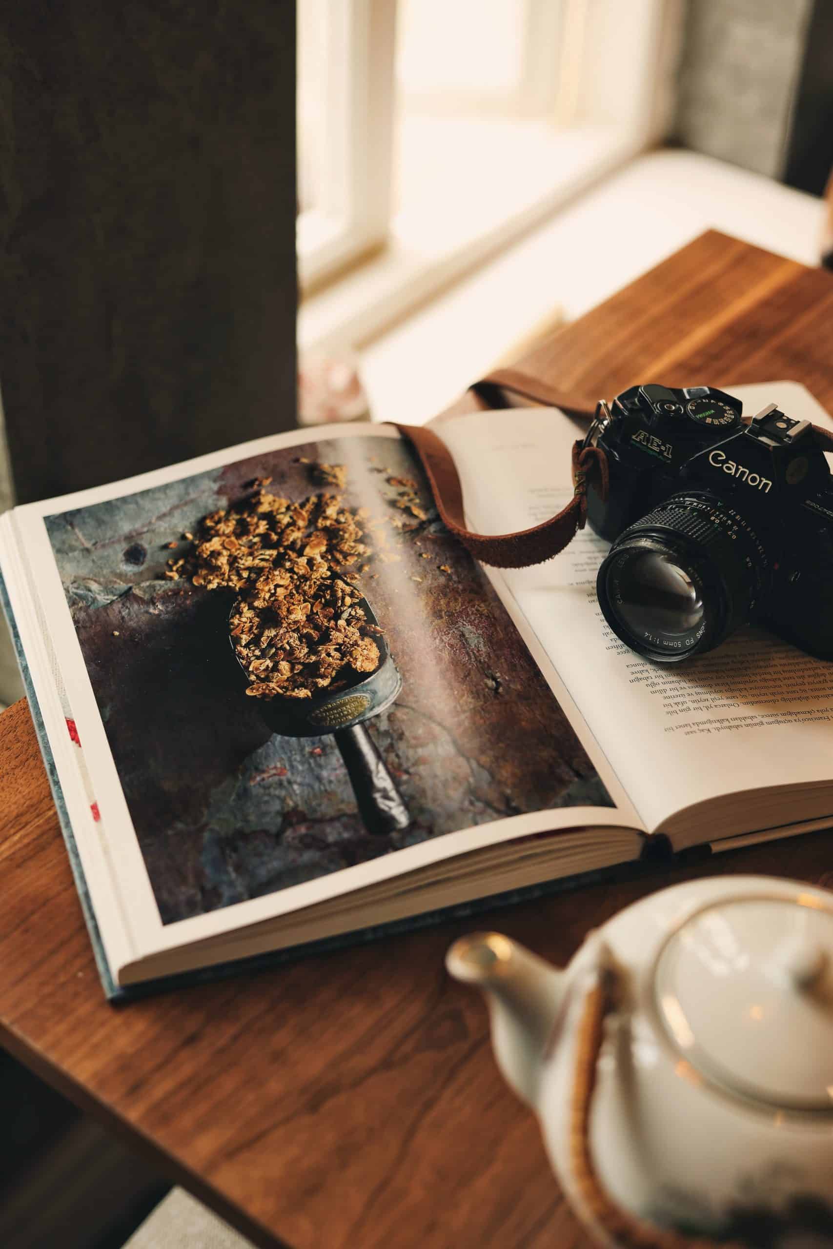 A cookbook laying open on a table with a camera.
