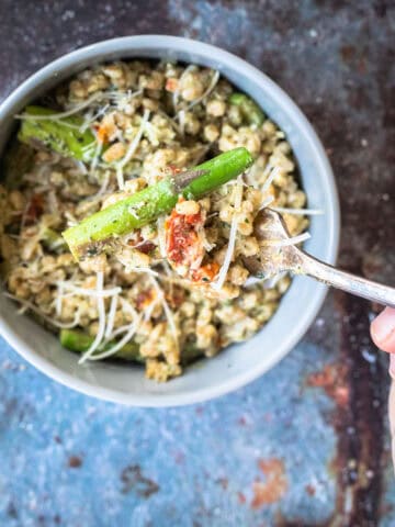 baked farro risotto with basil walnut pesto in a bowl with a spoon.