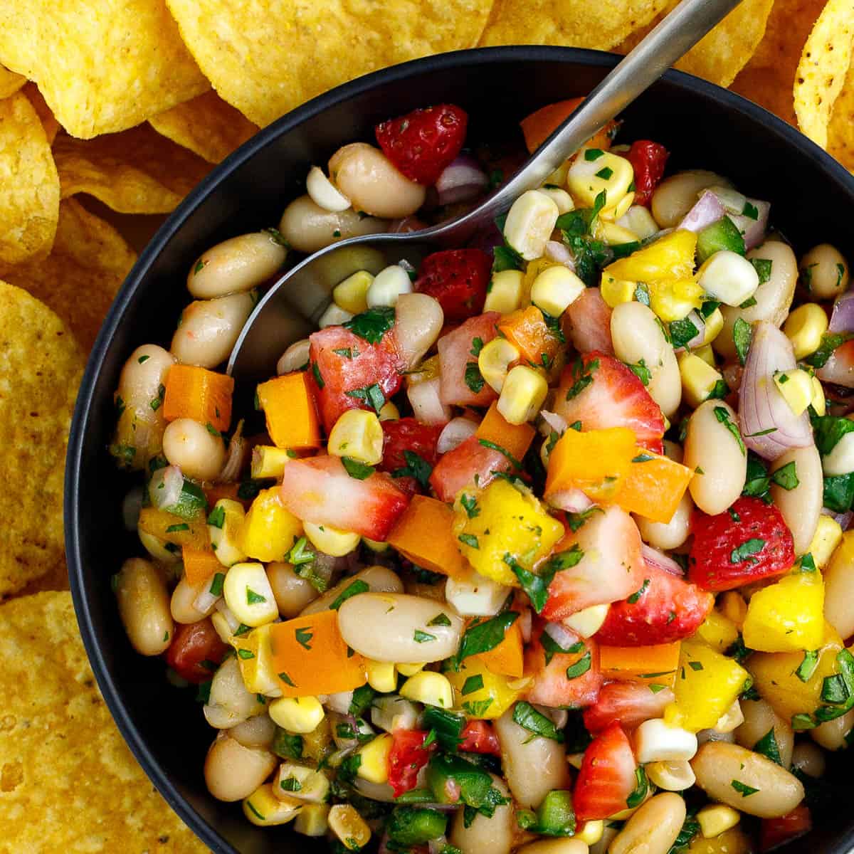 cowgirl caviar in a bowl with a spoon surrounded by chips.