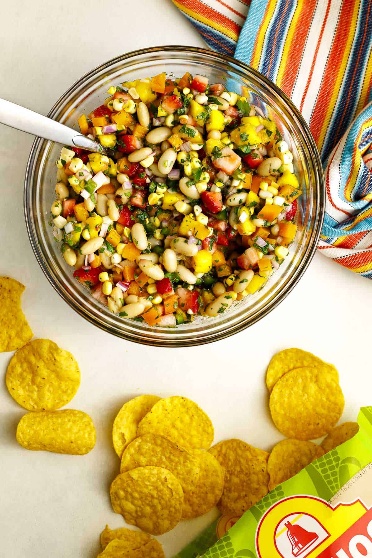 Cowgirl caviar with mango, strawberries, white beans, and corn in a bowl with chips on the side.