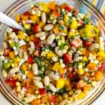 a bowl of cowgirl caviar with a spoon. Features strawberries, mangoes, red onions, and corn.