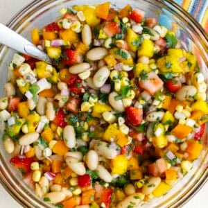 a bowl of cowgirl caviar with a spoon. Features strawberries, mangoes, red onions, and corn.
