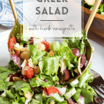 Loaded Greek salad in a bowl being tossed with salad tongs.