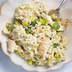 Risotto with chunks of chicken, green Castelvetrano olives, and leeks on a scalloped plate with a fork.