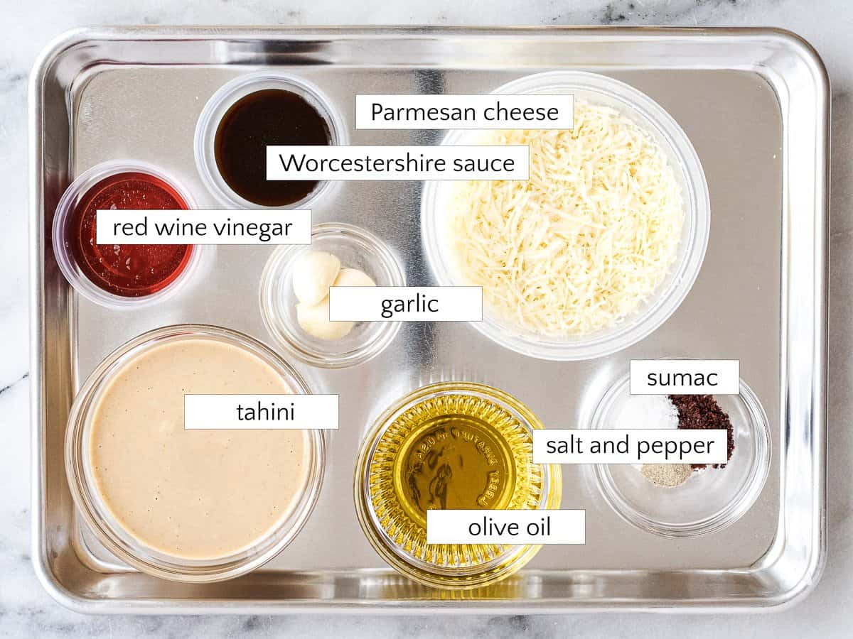 Ingredients for tahini Caesar salad dressing: Parmesan cheese, tahini, Worcestershire sauce, red wine vinegar, garlic, olive oil, salt and pepper, and sumac.