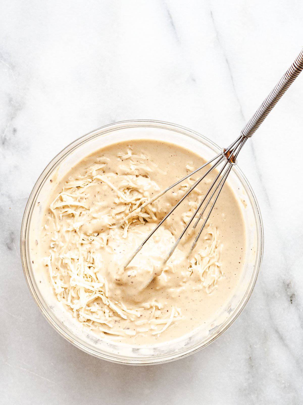 A bowl filled with tahini Caesar salad dressing and a whisk.