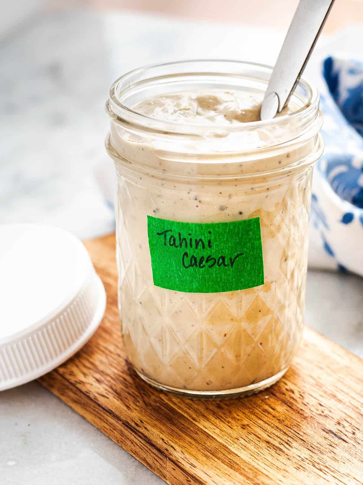 A mason jar with tahini Caesar dressing accompanied by a spoon and a lid.