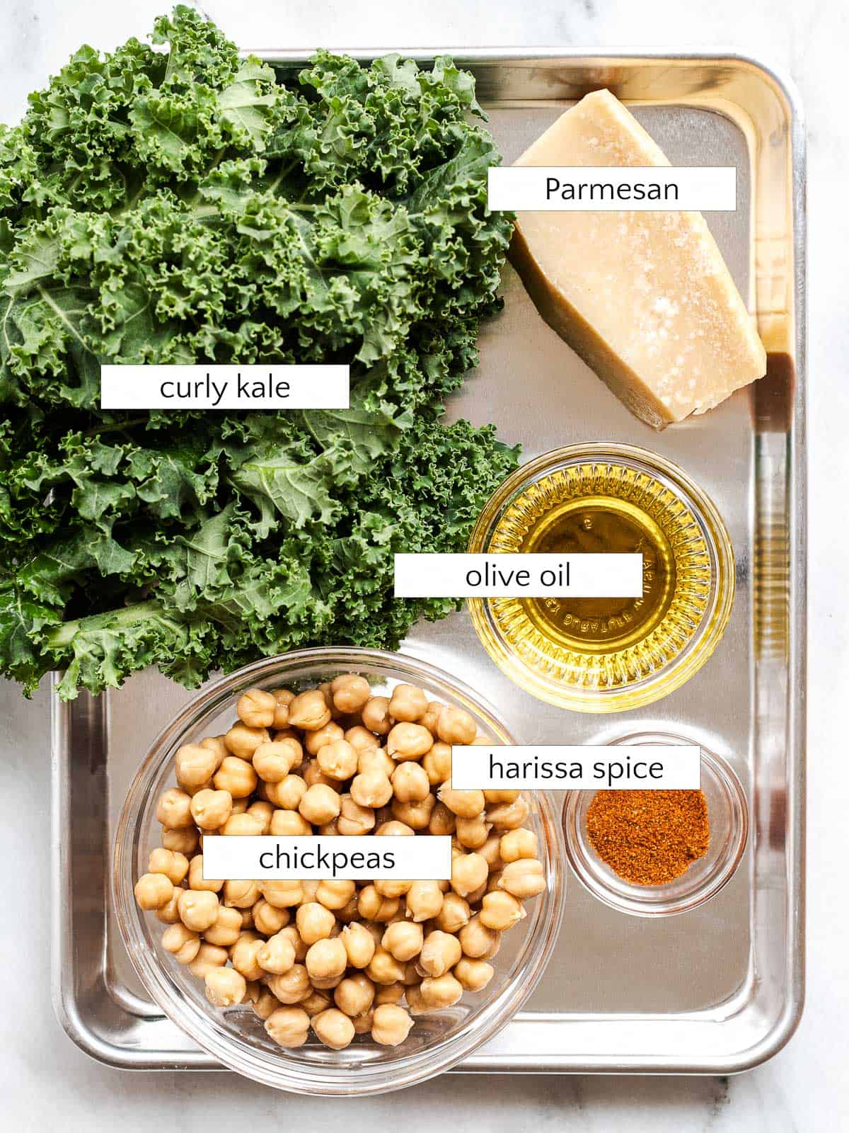 Ingredients for kale tahini Caesar salad: kale, Parmesan, olive oil, chickpeas, and harissa spice powder.