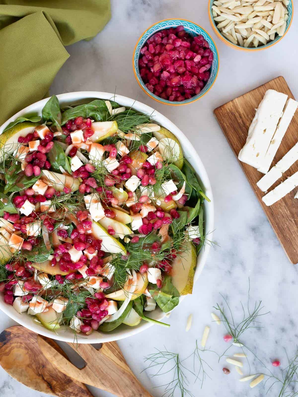 pear and fennel salad topped with feta cheese, almonds, and pomegranate arils. Drizzled with pomegranate vinaigrette. Served in a bowl with salad tongs and a napkin. Extra pomegranate, almonds, and feta cheese are served on the side.