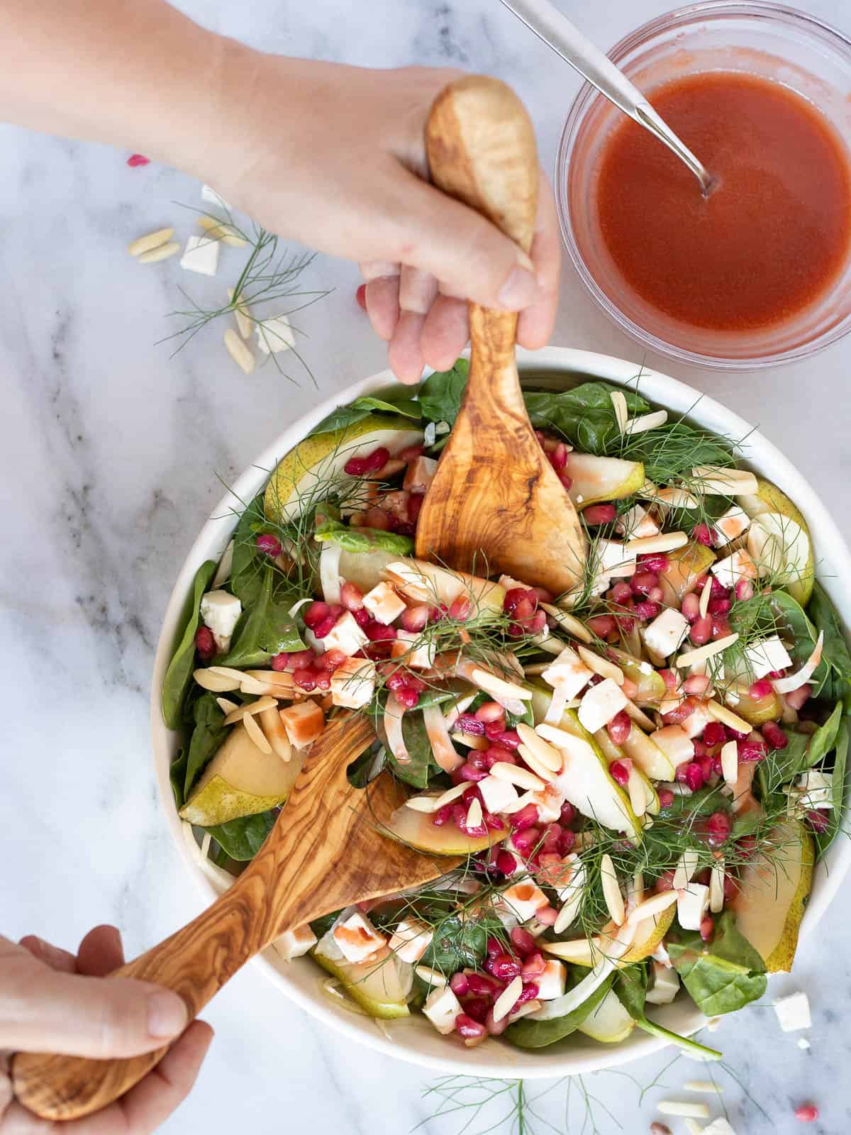 pear and fennel salad being tossed in a bowl with pomegranate vinaigrette.