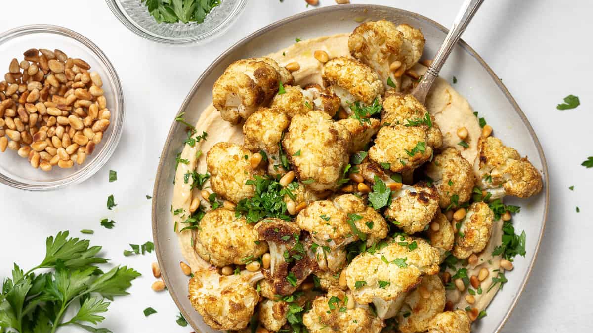 Roasted cauliflower coated with ground coriander served over a plate of hummus.