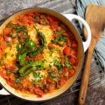 close up shot of blistered shishito pepper shakshuka with a serving utensil.