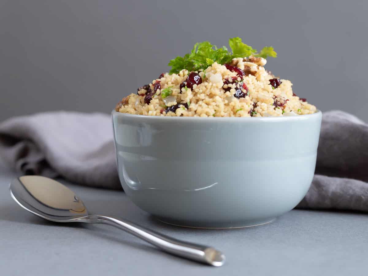 A bowl of cranberry walnut couscous with a napkin and a spoon.