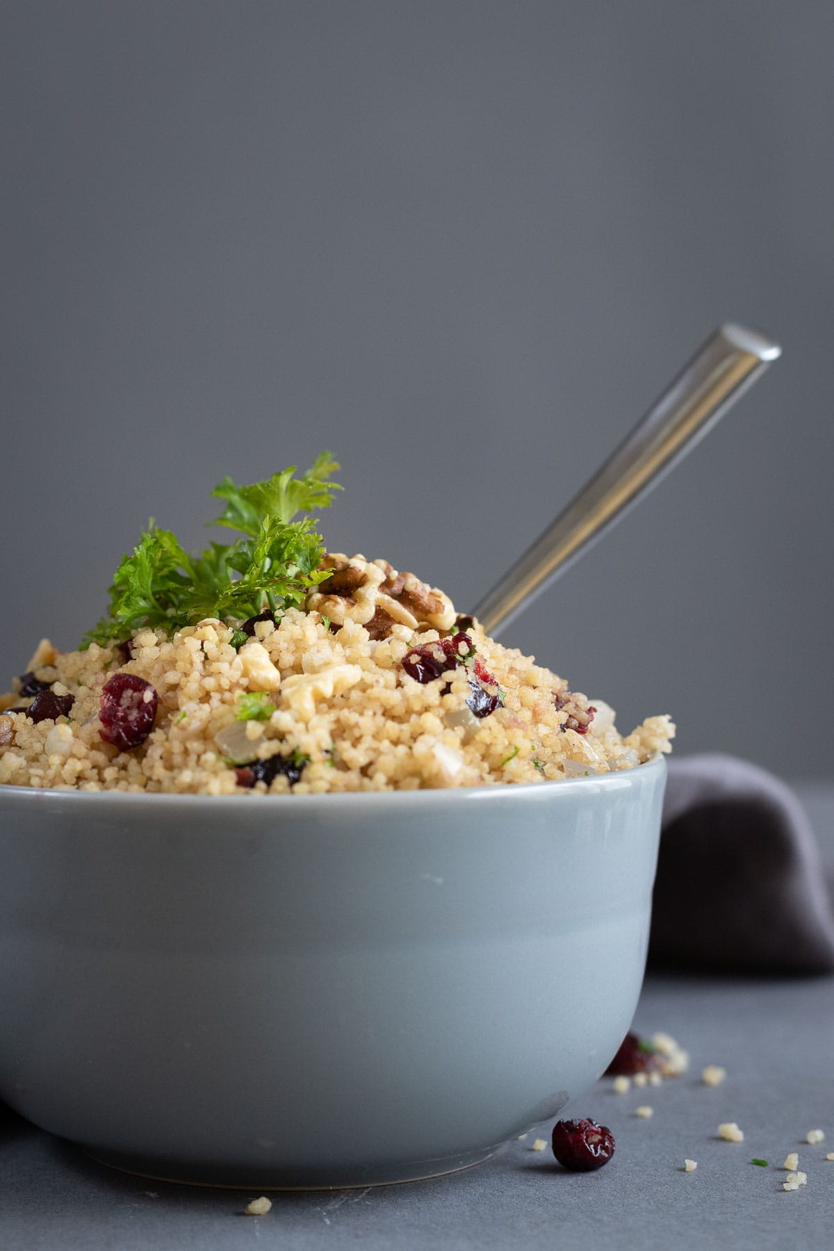 A bowl of whole wheat couscous studded with cranberries and walnuts and garnished with parsley.