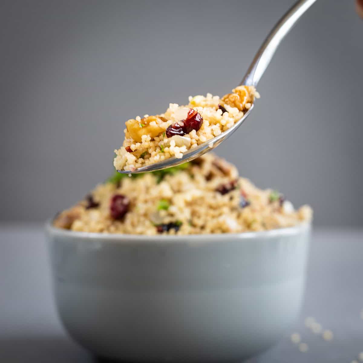 Spiced cranberry walnut couscous on a spoon with a bowl of couscous in the background.