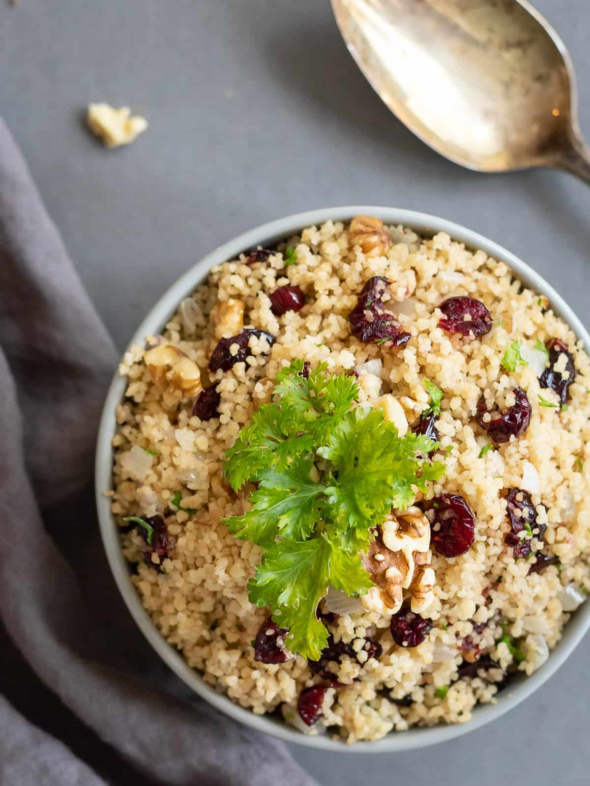 A bowl of whole wheat couscous with cranberries and walnuts garnished with parsley.