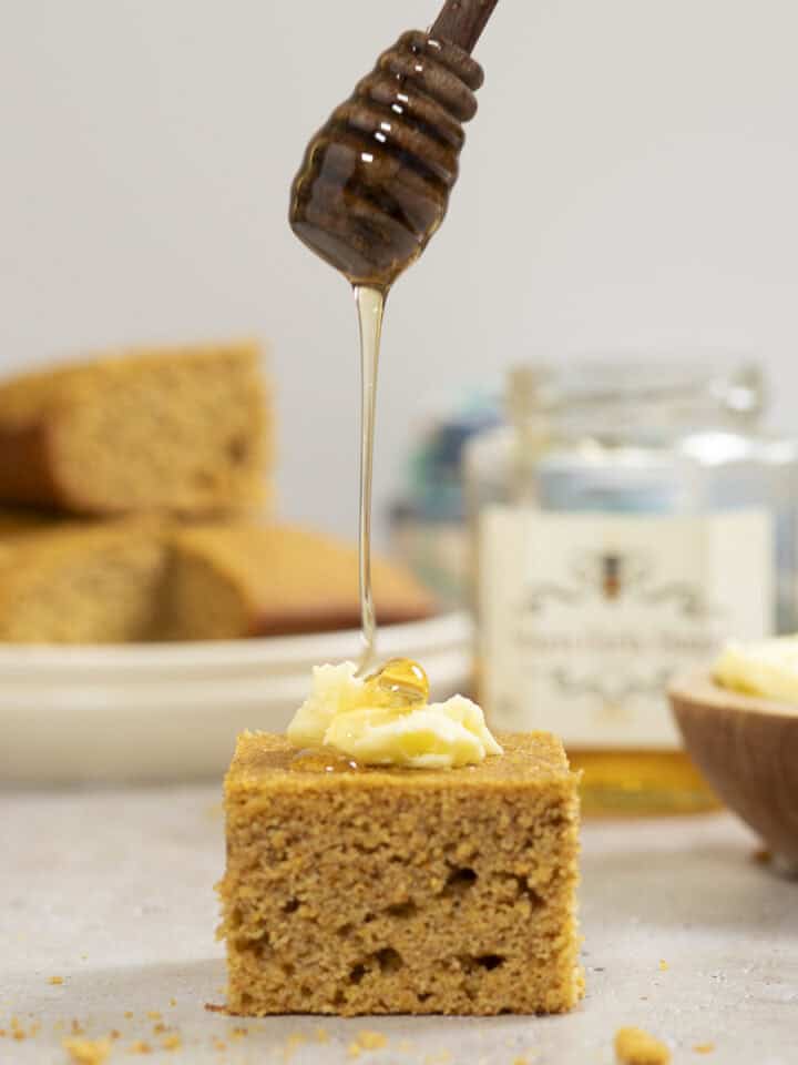 honey is drizzled on a piece of whole wheat cornbread topped with whipped butter.