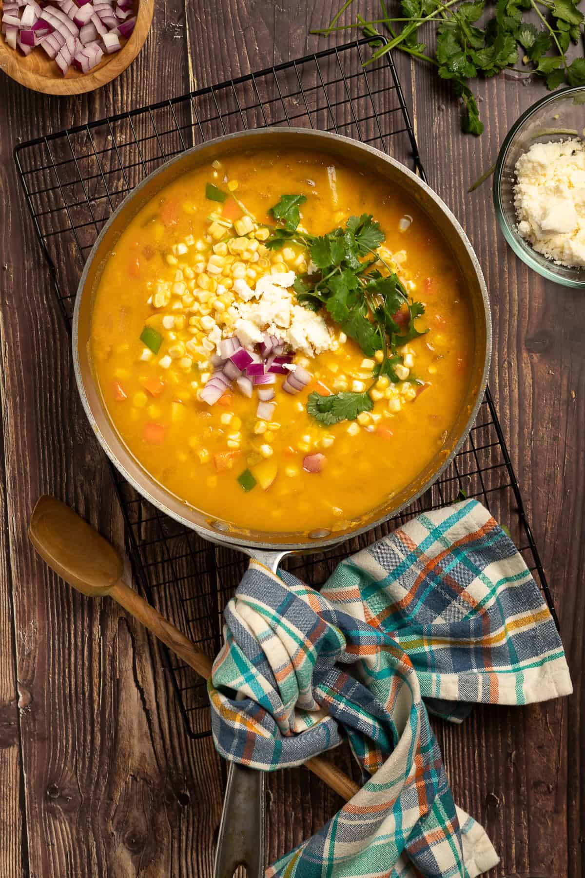 A saucepan with pumpkin poblano corn chowder sits on a wire rack with a spoon and a napkin nearby.