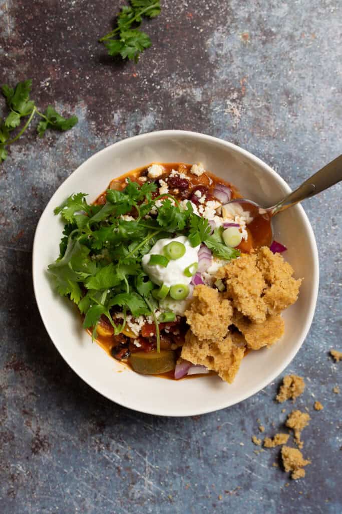 A vegetarian chili recipe is shown topped with cilantro, plain yogurt, cornbread, and sliced red and green onions.