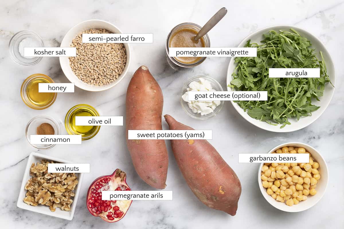 Ingredients for farro and arugula salad with sweet potatoes and pomegranate: semi-pearled farro, kosher salt, honey, olive oil, arugula, goat cheese, cinnamon, sweet potatoes, garbanzo beans, pomegranate arils, walnuts, and pomegranate vinaigrette.