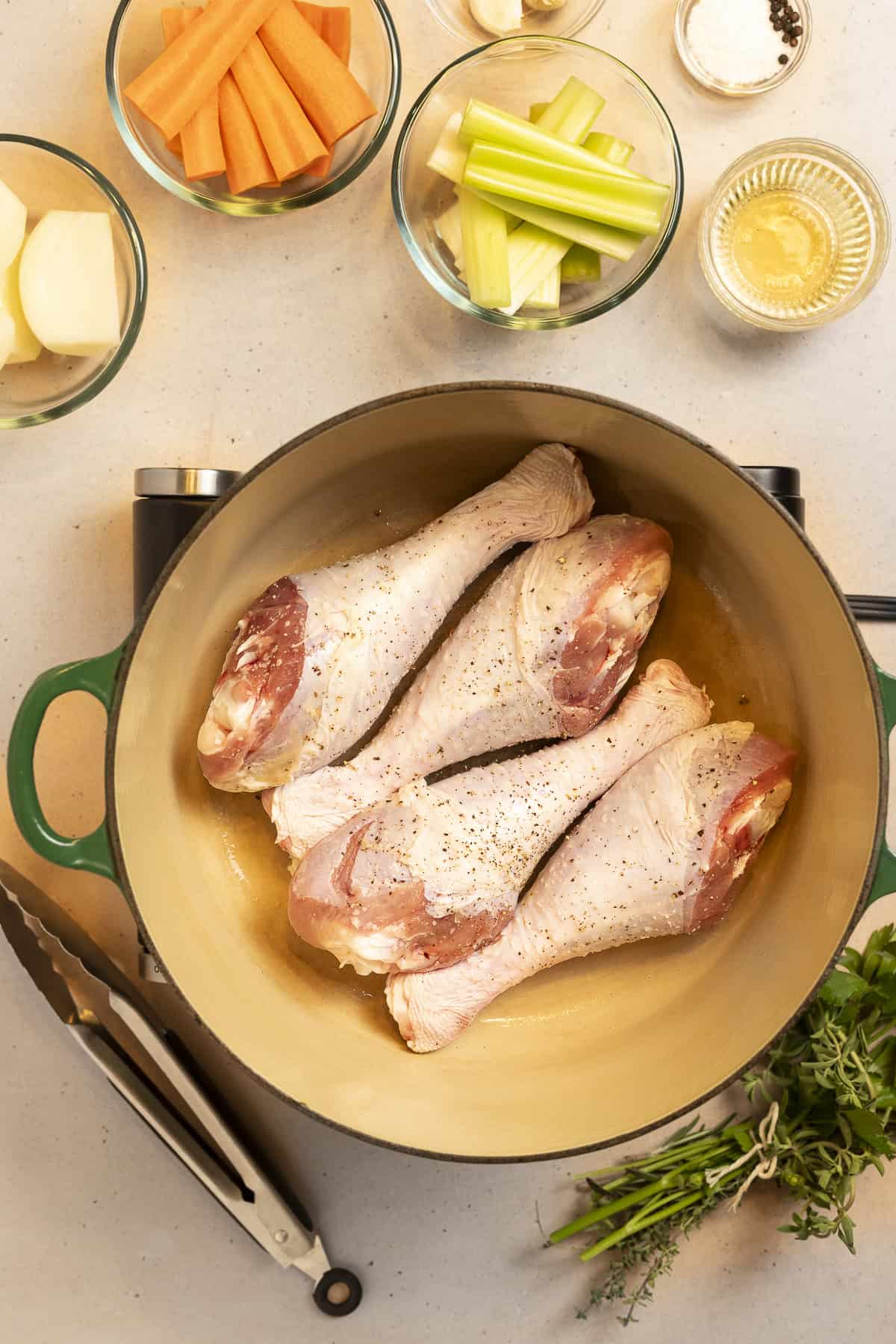 Turkey legs brown in a pan for turkey broth. Onion, carrots, garlic, and wine sit on the counter waiting to be added.