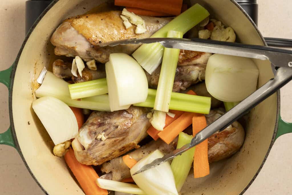 after browning, turkey legs are added back to the pan along with aromatic vegetables and herbs