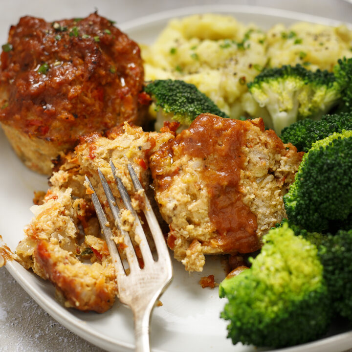 A muffin pan turkey meatloaf is cut in half with a fork and sits on a plate with broccoli and mashed potatoes.