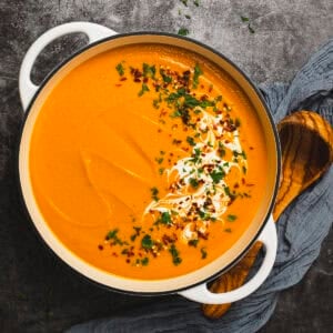Spiced carrot and red lentil soup in a pot with a ladle and napkin.