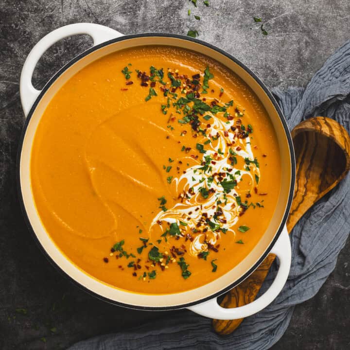 Spiced carrot and red lentil soup in a pot with a ladle and napkin.