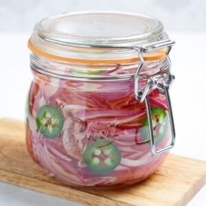 A closed jar of spicy quick pickled onions sits on a cutting board.