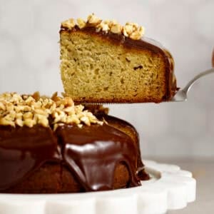 A piece of banana olive oil cake is lifted by a spatula for serving.