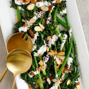 Broccolini on a plate topped with yogurt sauce, almonds, and sumac.