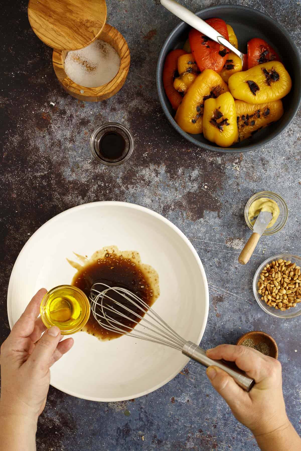 olive oil is whisked into balsamic vinegar and olive oil in a salad bowl. 