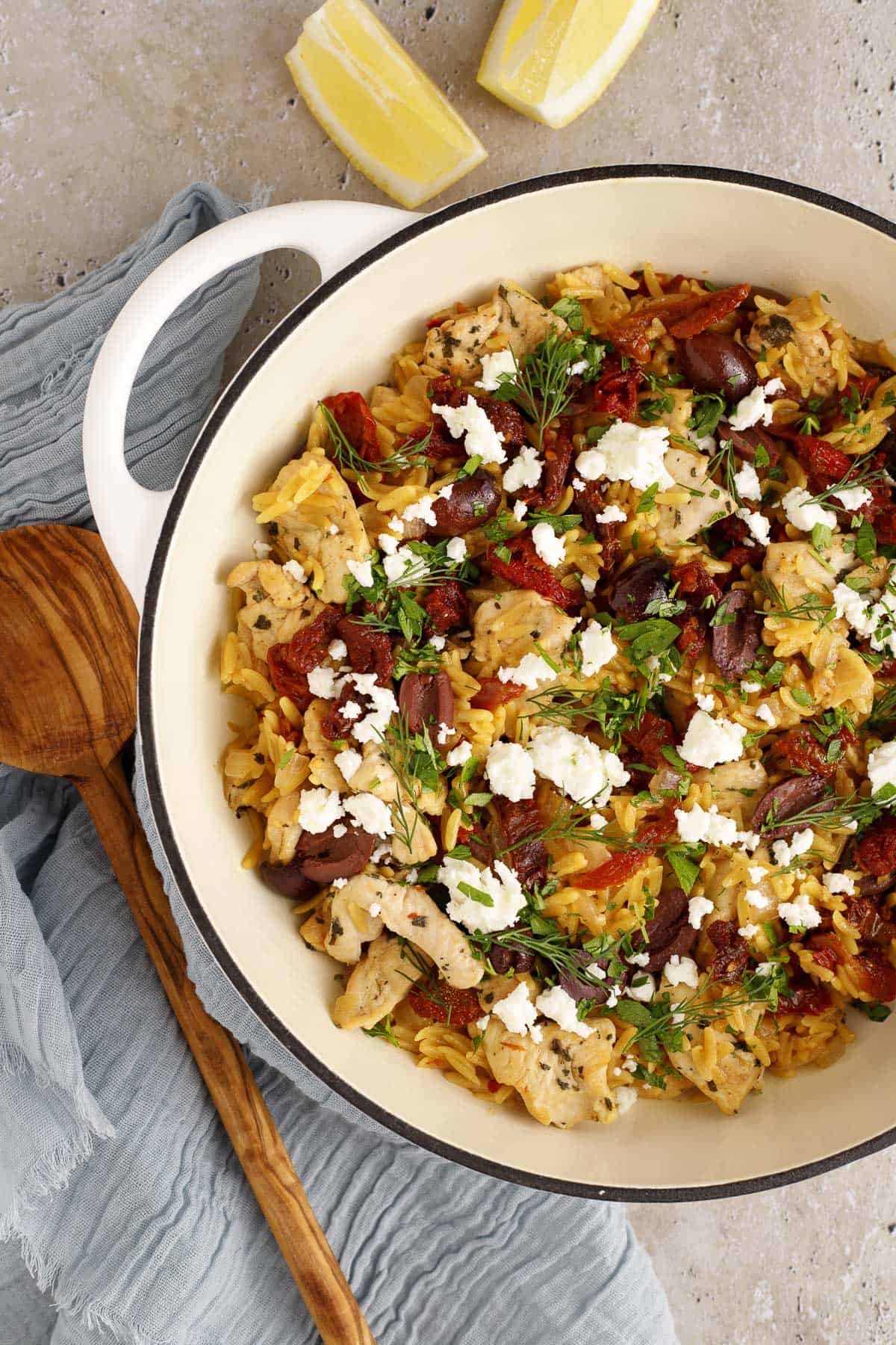 Mediterranean chicken and orzo skillet in a pan with a spoon and lemon wedges