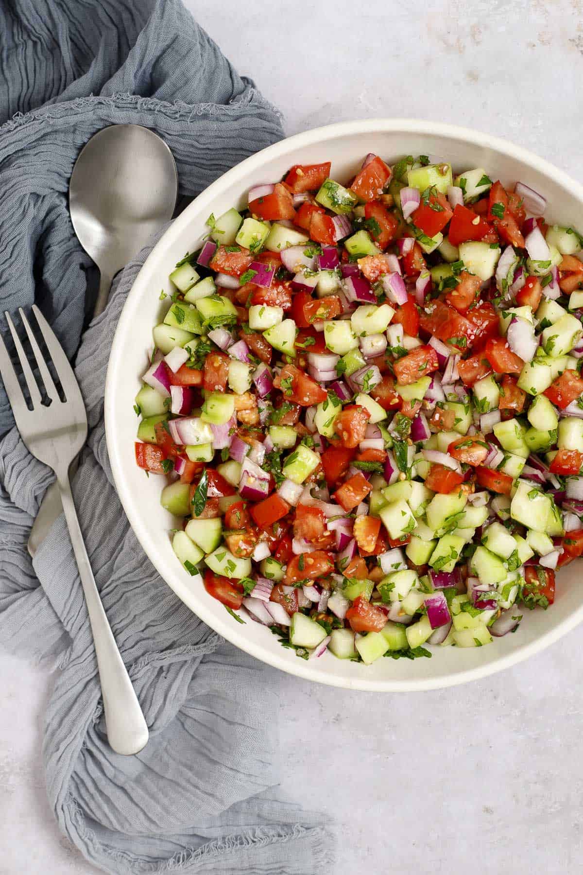 A bowl of Mediterranean chopped salad in a bowl with salad serving utensils.