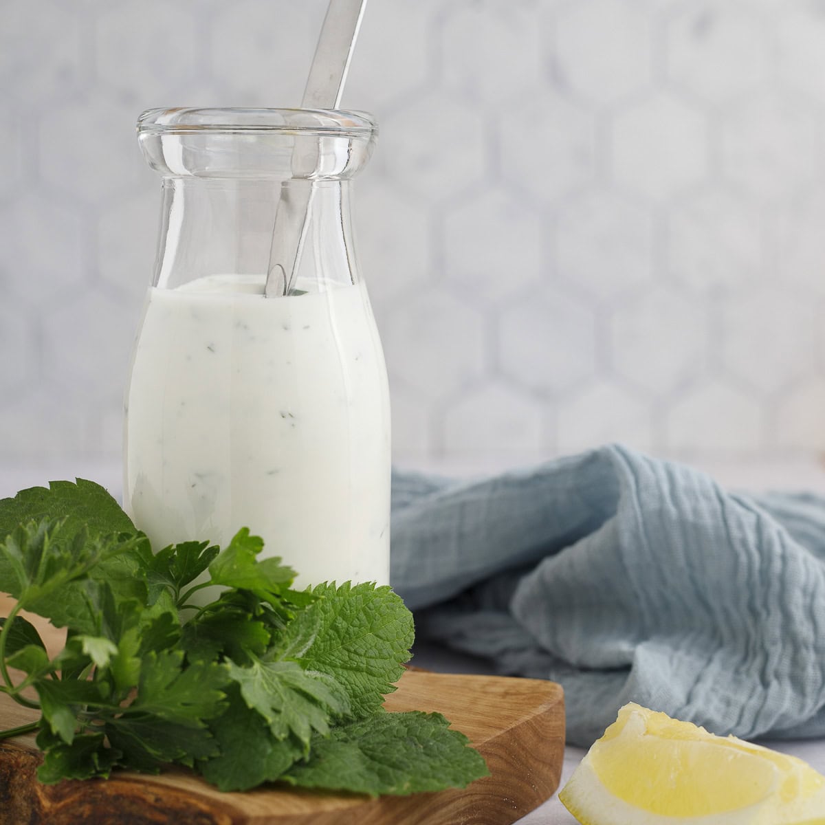 yogurt sauce in a bottle with a spoon and a napkin. Herbs and lemons sit in the foreground.