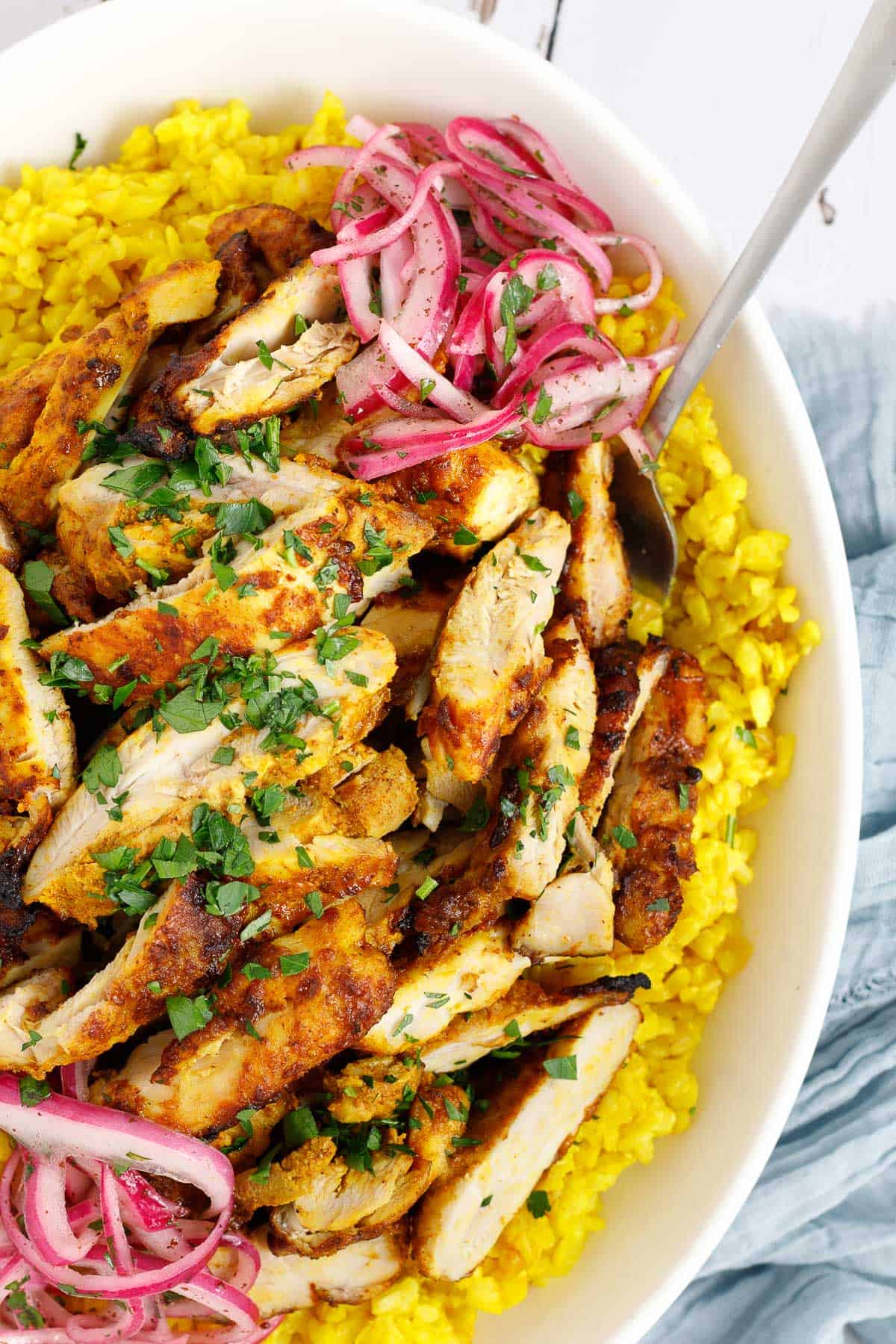 Air fryer chicken shawarma is sliced and served over Mediterranean yellow rice in a bowl with a spoon. It is accompanied by sumac onions. 