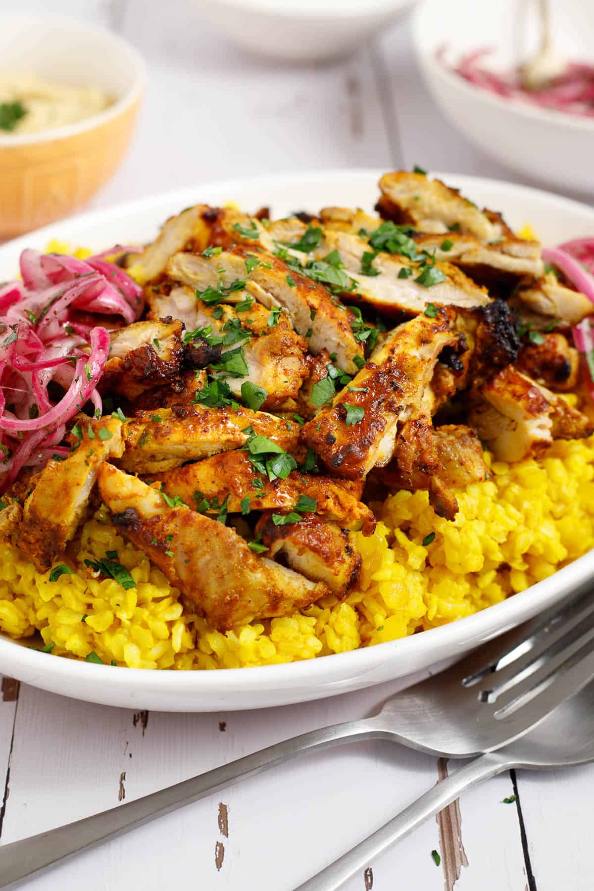 chicken shawarma piled over Mediterranean yellow rice, accompanied by sumac onions on a platter.