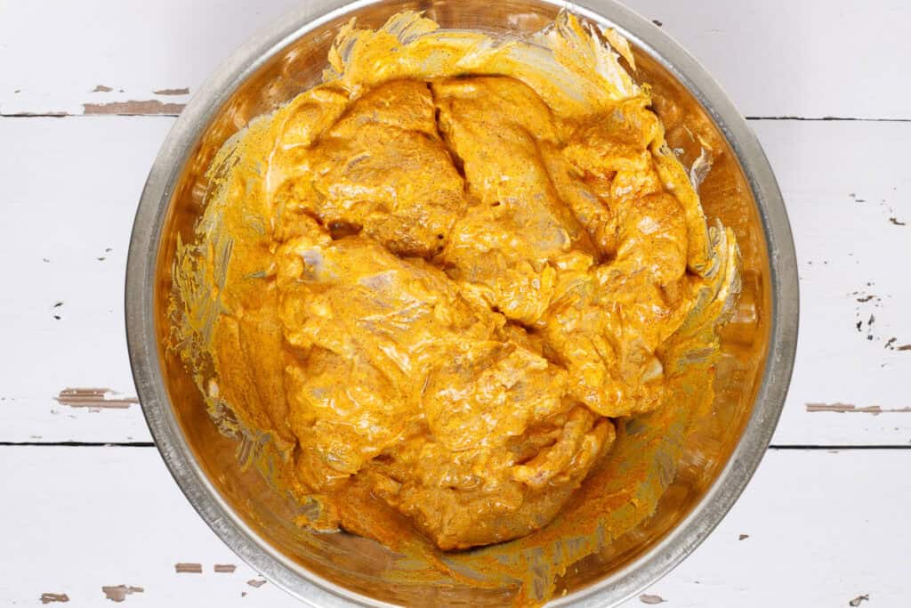 Chicken thighs are shown in a bowl mixed with chicken shawarma marinade.