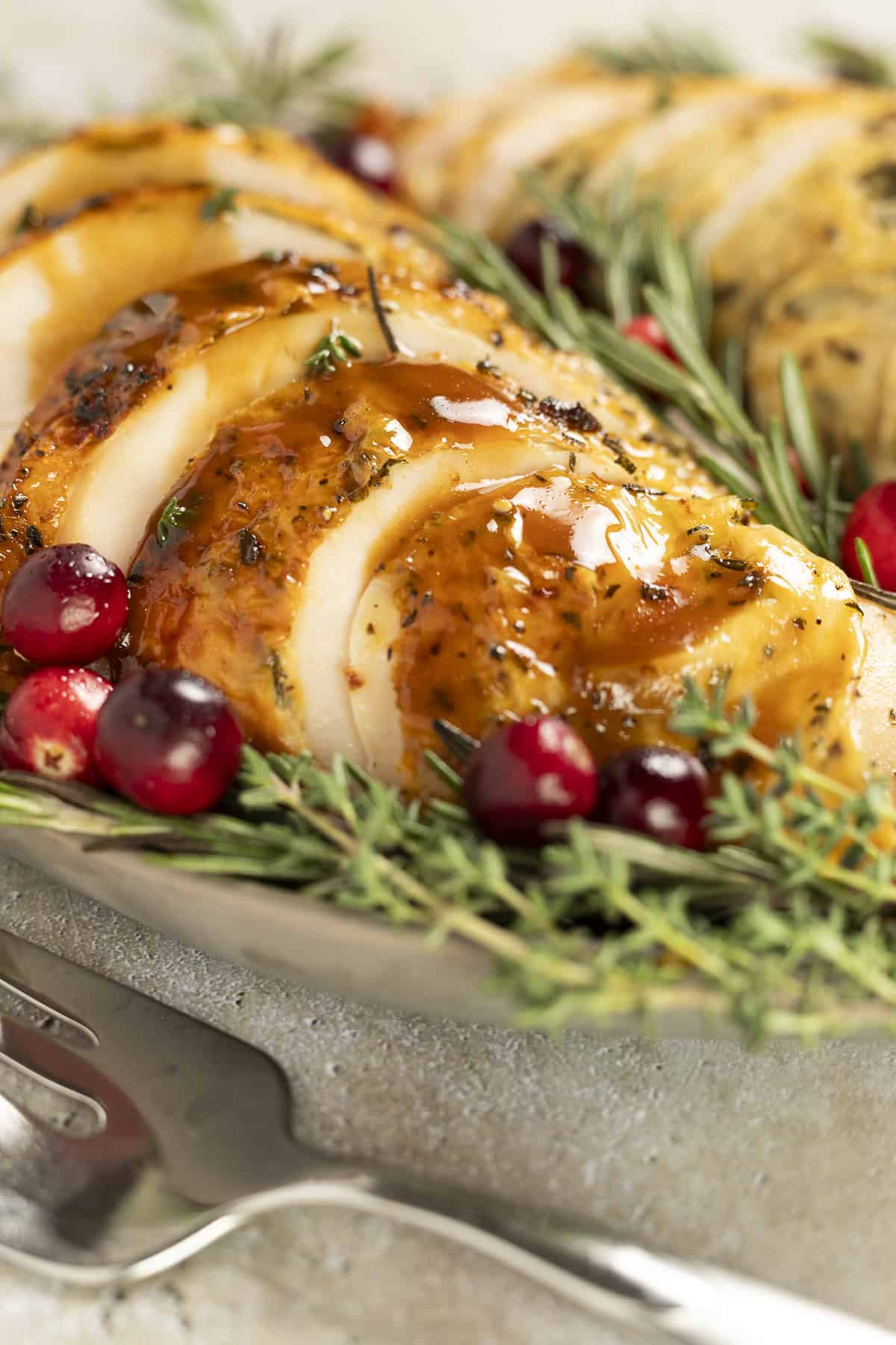 Pan-roasted turkey breast on a platter with balsamic gravy. Garnished with rosemary and cranberries. A serving fork sits nearby.