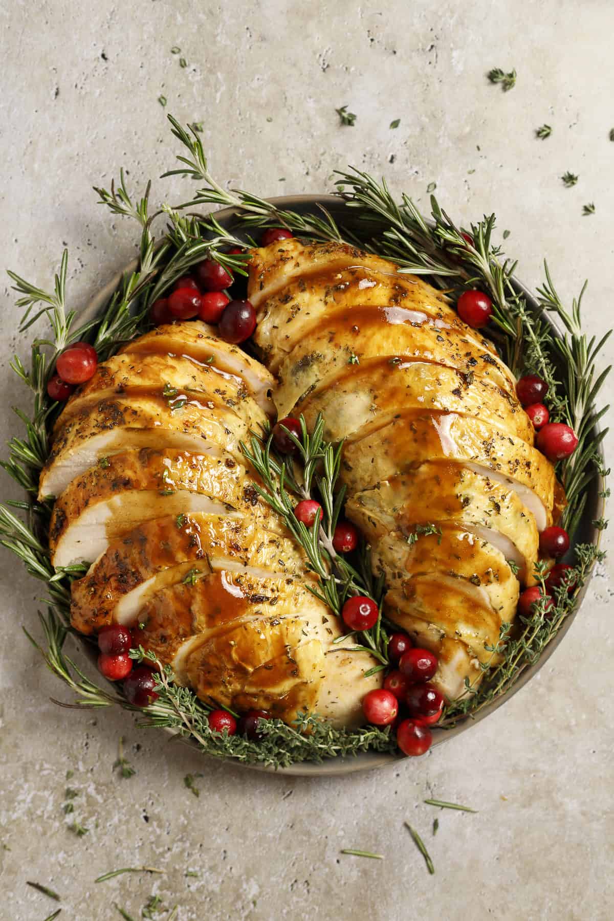 Two turkey breasts with golden brown skin are laid out on a platter and drizzled with balsamic gravy. They are garnished with rosemary and cranberries.