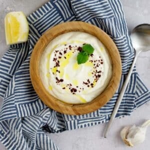 Lemon garlic yogurt sauce in a bowl garnished with sumac and mint.